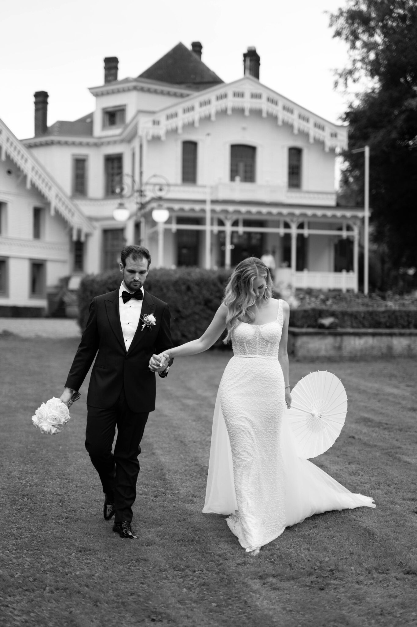Braut und Bräutigam spazieren Hand in Hand vor einem großen historischen Haus, gekleidet in Hochzeitskleidung - ein unvergesslicher Moment, wunderschön inszeniert von einem Hochzeitsplaner Italien Spezialist.