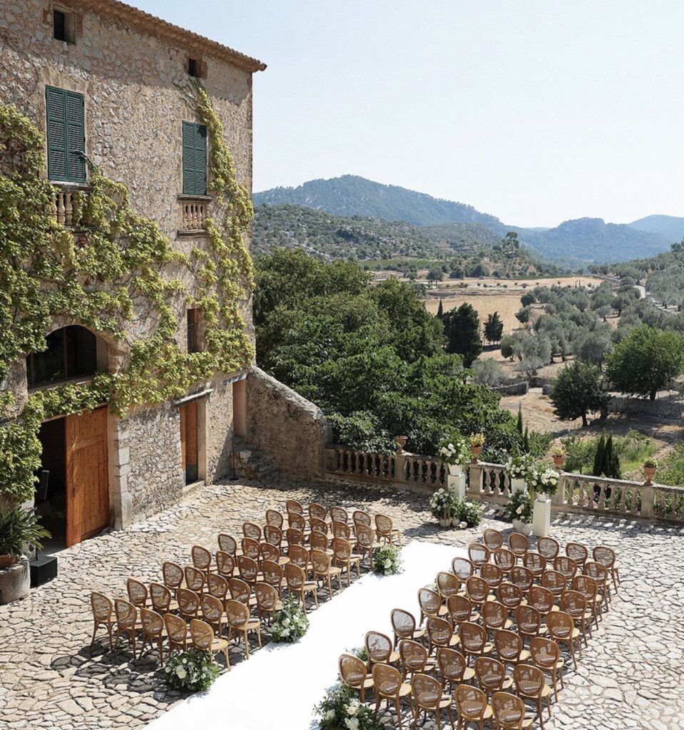 Aufbau für eine Hochzeitszeremonie im Freien mit Stuhlreihen und Blumen neben einer rustikalen Hochzeitslocation auf Mallorca.