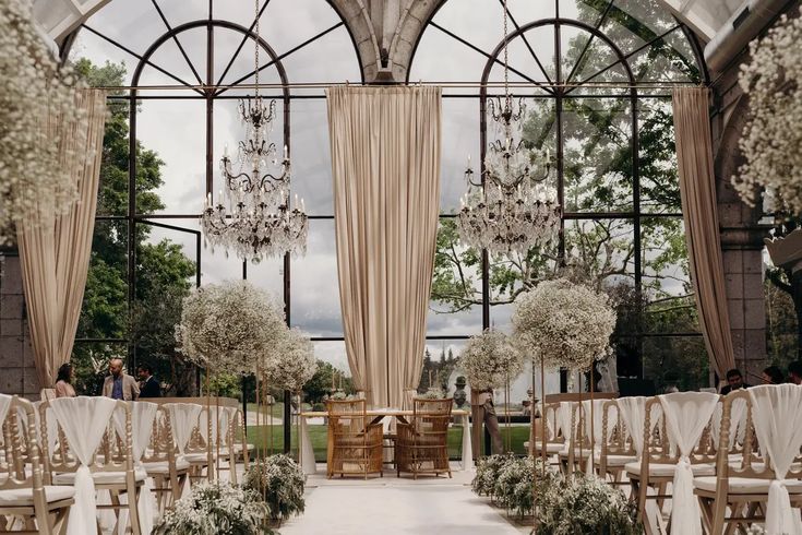 Elegante Hochzeit im Innenbereich mit Kronleuchtern, drapierten Vorhängen und weiß geschmückten Stuhlreihen vor einem Altar.