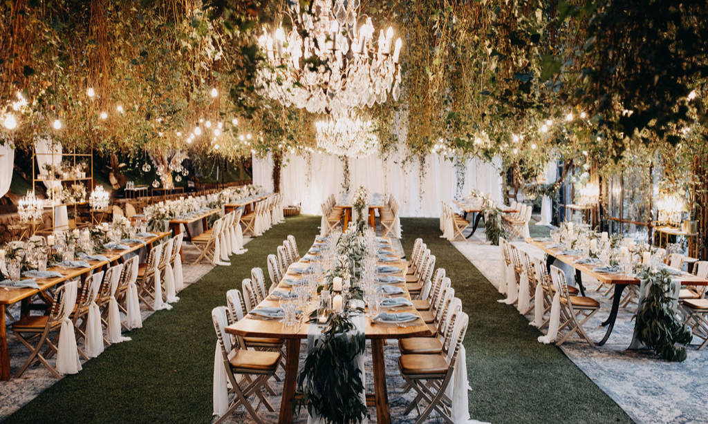 Eleganter Hochzeitsempfang mit langen Holztischen, hängenden Grünpflanzen, Kronleuchtern und Lichterketten.