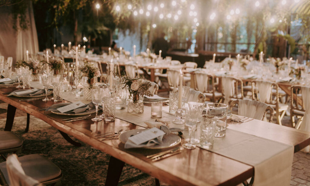 Eleganter Banketttisch für eine Veranstaltung mit Gläsern, Kerzen und Blumen unter Lichterketten.