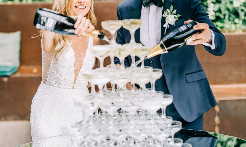 Braut und Bräutigam gießen während ihrer Hochzeitsfeier Champagner in einen Turm von Gläsern.