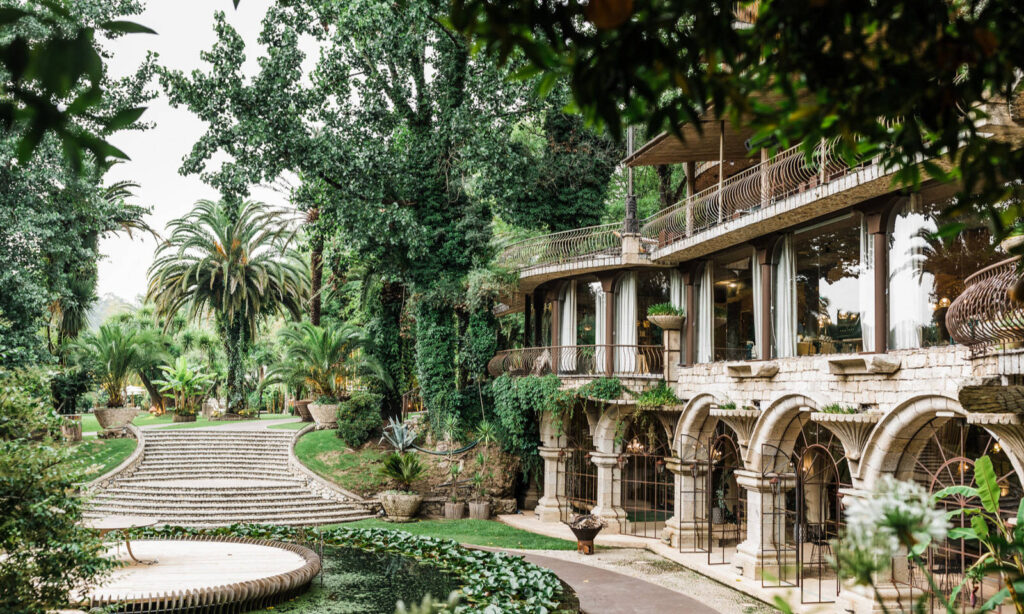 Das elegante Steingebäude mit Bogenfenstern bietet einen Blick auf üppige Gärten, Palmen und einen Teich mit Seerosenfeldern.