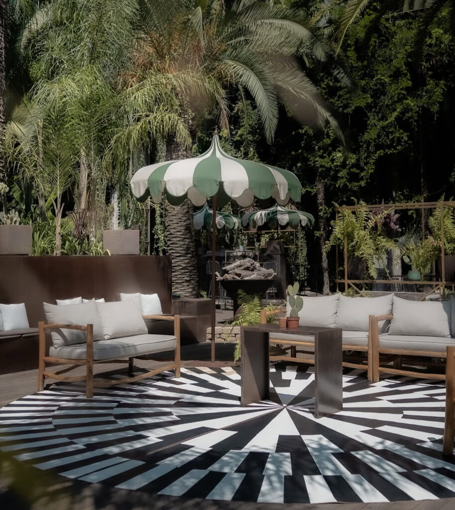 Eine Außenterrasse mit hölzernen Sitzgelegenheiten, einem grün-weißen Sonnenschirm und einem kühnen schwarz-weißen Teppich - perfekt zum Entspannen oder als stilvolle portugiesische Hochzeitslocation, kuratiert von einem erfahrenen Hochzeitsplaner.
