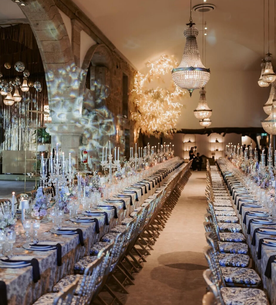 Lange Banketttische mit eleganten Gedecken, hohen Kerzen, Kronleuchtern und kunstvollen Blumenarrangements schaffen eine atemberaubende Hochzeitslocation - perfekt für eine portugiesische Hochzeit, die von einem erfahrenen Hochzeitsplaner geplant wurde.