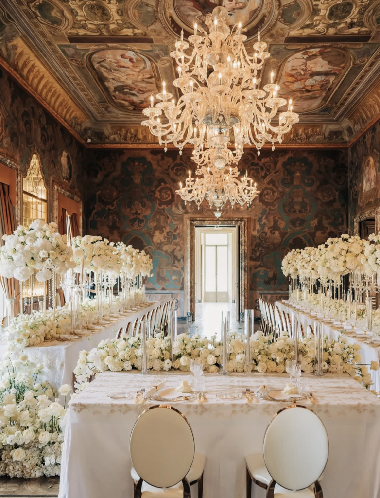 Ein prunkvoller Ballsaal mit Kronleuchtern, Blumenschmuck und eleganter weißer Tischdekoration – perfekt für eine luxuriöse Hochzeit im Ausland oder für alle, die nach exquisiten Hochzeitslocations am legendären Comer See suchen.