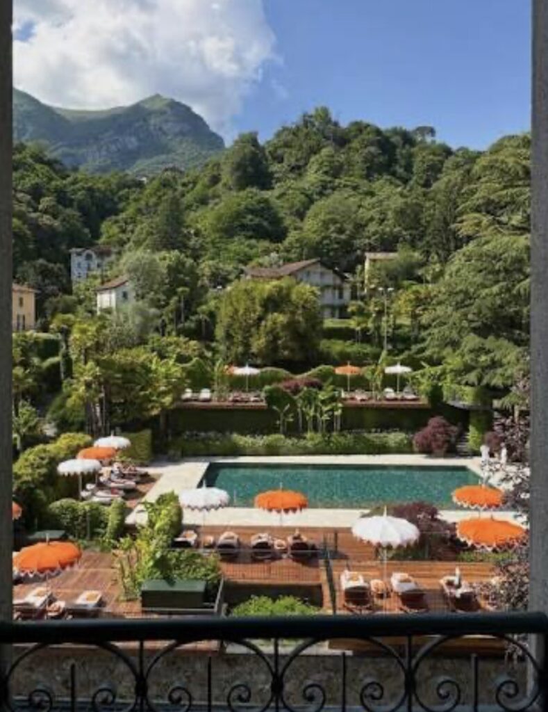 Ein Pool mit orangefarbenen Sonnenschirmen und Liegestühlen, umgeben von üppigem Grün und mit den Bergen im Hintergrund – eine idyllische Kulisse, perfekt für eine luxuriöse Hochzeit im Ausland oder eine unvergessliche Hochzeit am Comer See.