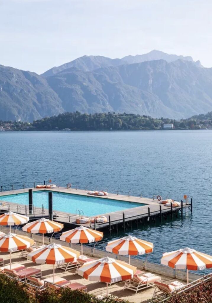 Orangefarbene und weiße Sonnenschirme an einem Pool am Seeufer, mit Bergen und Wasser im Hintergrund, schaffen eine idyllische Kulisse, die sich perfekt für eine luxuriöse Hochzeit im Ausland eignet oder für alle, die nach exquisiten Hochzeitslocations für ihre Hochzeit am Comer See suchen.