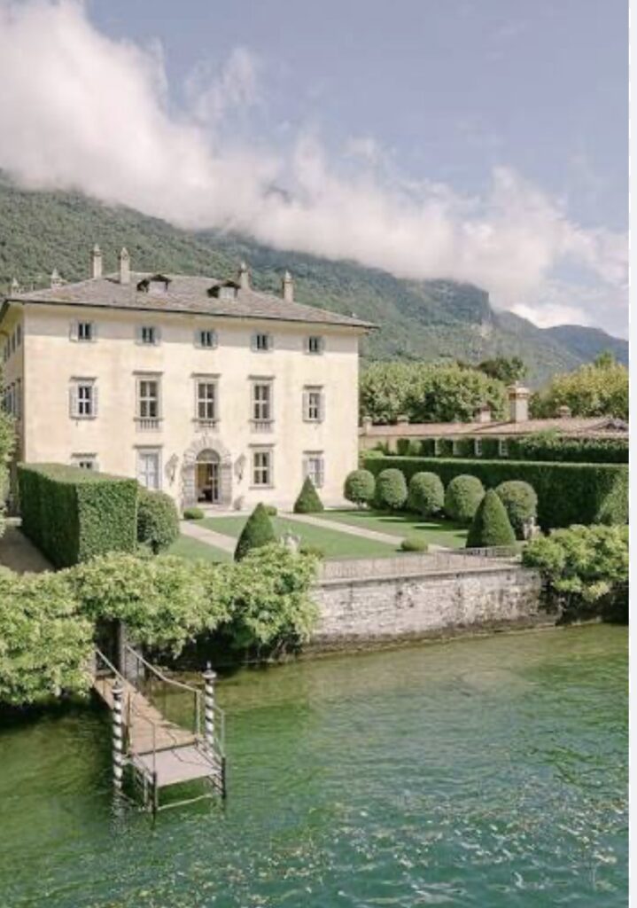 Eine elegante Villa mit gepflegten Gärten, einem Bootsanleger und den Bergen im Hintergrund, direkt an einem klaren, grün schimmernden See gelegen – eine exquisite Hochzeitslocation für eine luxuriöse Hochzeit im Ausland oder eine unvergessliche Hochzeit am Comer See.