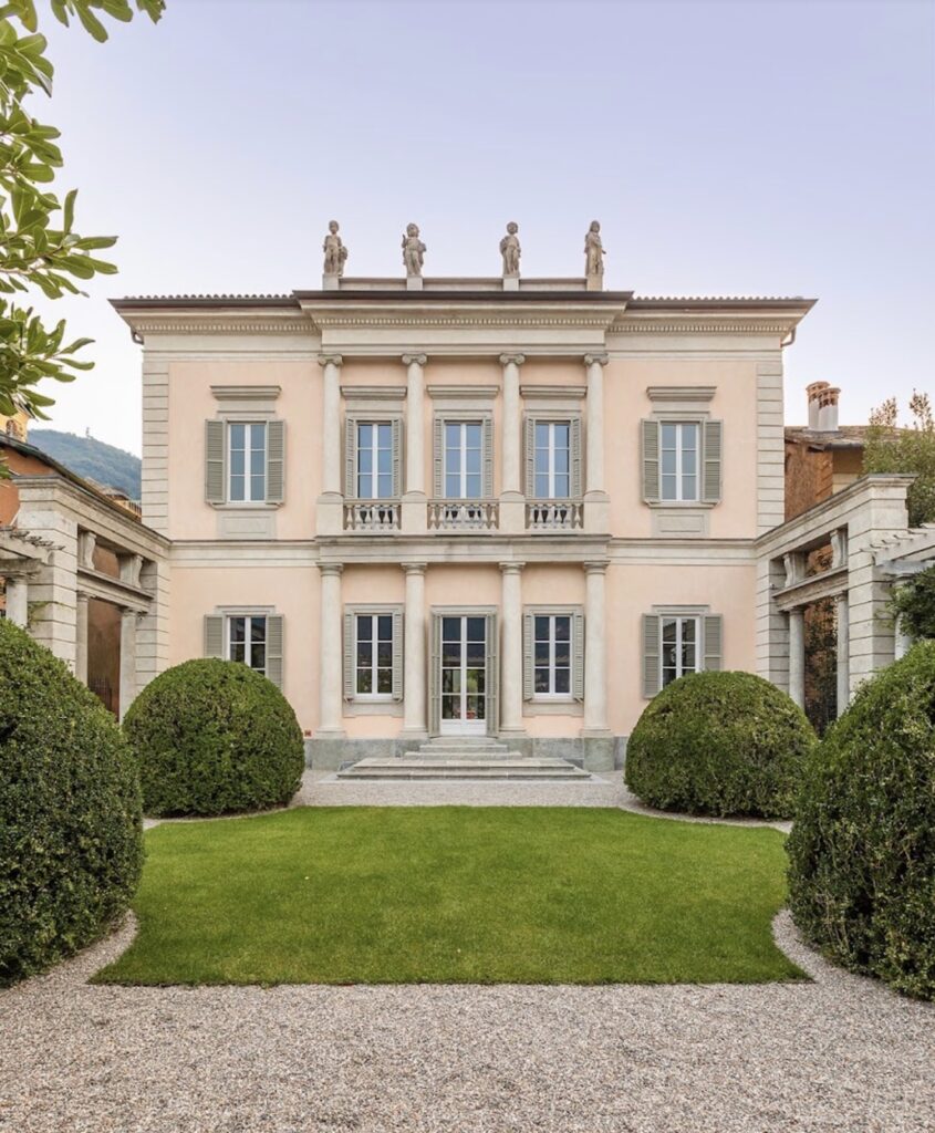 Eine neoklassizistische Villa mit Säulen, Statuen auf dem Dach und einem gepflegten grünen Rasen davor – ein idealer Ort für eine luxuriöse Hochzeit am Comer See, perfekt für Paare, die nach exklusiven Hochzeitslocations mit zeitloser Eleganz suchen.