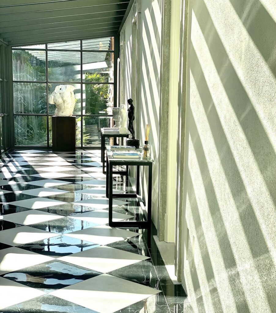 Ein sonnendurchfluteter Flur mit schwarz-weißem Fliesenboden, modernen Skulpturen und großen Fenstern, die gestreifte Schatten werfen – ein Ambiente, das an eine luxuriöse Hochzeit im Ausland oder an eine der eleganten Hochzeitslocations für eine Hochzeit am Comer See erinnert.