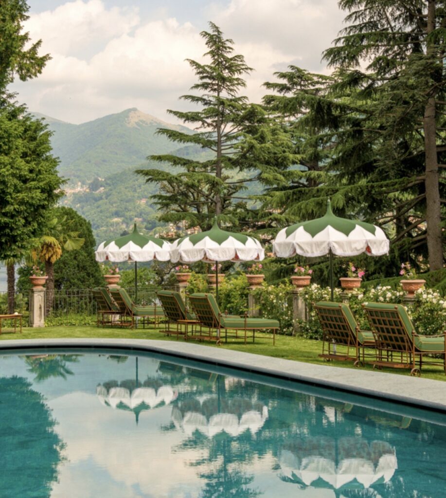 Am Pool mit grünen und weißen Sonnenschirmen, Liegestühlen und Blick auf die Berge, umgeben von üppigen Bäumen und Blumen – eine idyllische Kulisse, perfekt für eine luxuriöse Hochzeit im Ausland oder eine unvergessliche Hochzeit am Comer See.