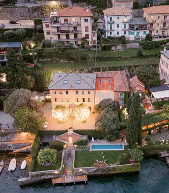 Luftaufnahme einer eleganten Villa mit Gärten, einem Pool und Booten am Seeufer am Abend – eine idyllische Kulisse für eine luxuriöse Hochzeit im Ausland oder für alle, die auf der Suche nach exquisiten Hochzeitslocations am Comer See sind.