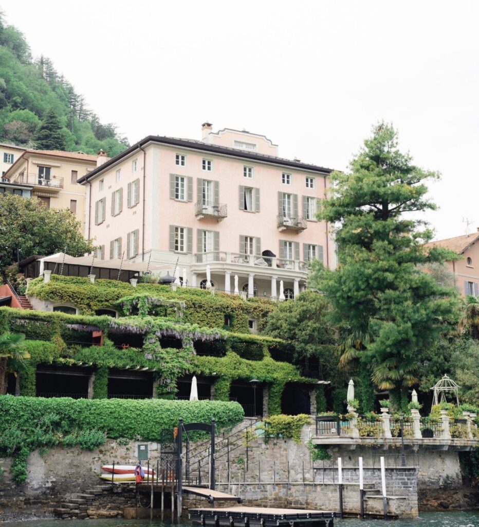 Große rosafarbene Villa mit Balkonen, üppiger Vegetation, Terrassen und einem kleinen Steg am Wasser – ideal für eine luxuriöse Hochzeit im Ausland oder als einer der bezauberndsten Hochzeitsorte für Ihre Hochzeit am Comer See.