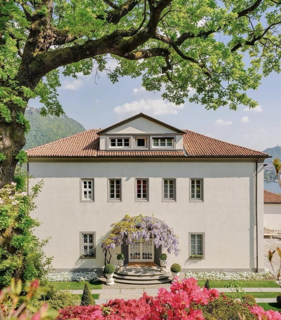 Eine weiße Villa mit rotem Ziegeldach, Glyzinienranken und farbenprächtigen Gartenblumen vor dem Haus – dieser bezaubernde Rückzugsort ist einer der begehrtesten Hochzeitsorte für eine luxuriöse Hochzeit am Comer See.