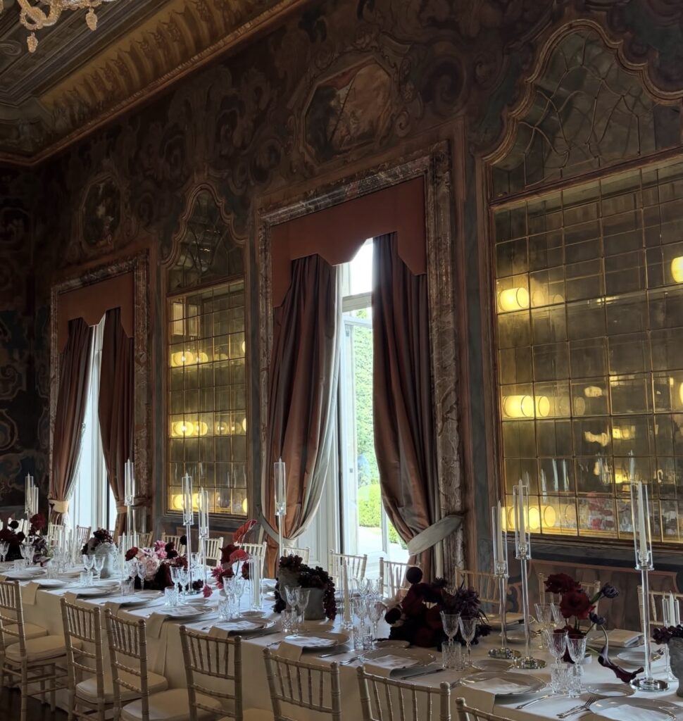 Ein elegantes Esstisch-Set mit Blumen und Kerzen in einem prächtigen Raum der Villa Erba, dessen hohe Fenster und kunstvoll verzierte Spiegel den zeitlosen Charme des Comer Sees widerspiegeln.