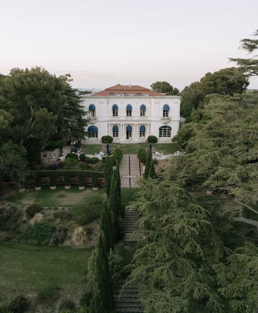 Ein großes weißes Herrenhaus mit hohen Fenstern, umgeben von üppigen Gärten und hohen Bäumen, aus der Vogelperspektive betrachtet – ein atemberaubender Blick auf die Villa Rocabella, ein traumhafter Ort für eine Hochzeit an der Côte d’Azur.