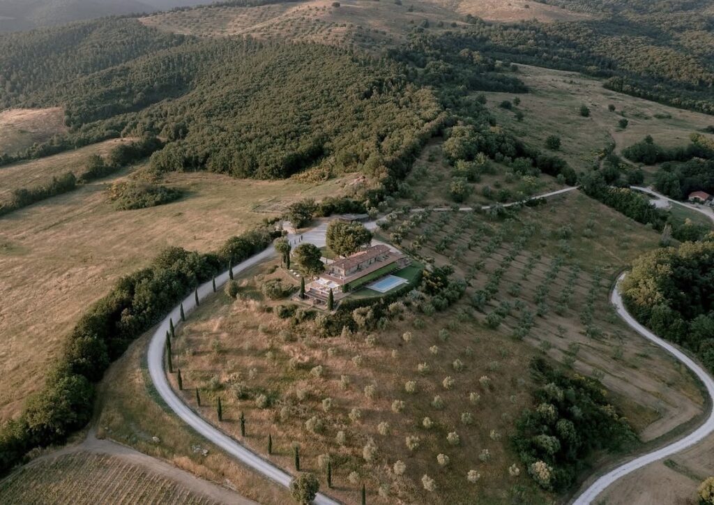Luftaufnahme einer Villa mit Pool, umgeben von Bäumen und kurvenreichen Straßen in einer hügeligen Landschaft – einer der schönsten Orte für ein unvergessliches Hochzeitserlebnis in der Toskana.
