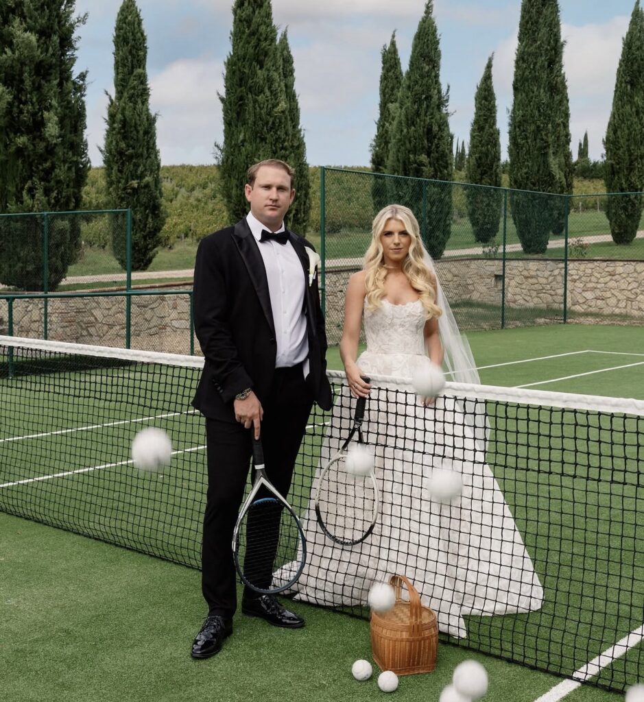 Braut und Bräutigam posieren in Hochzeitskleidung auf einem Tennisplatz, halten Schläger in den Händen, während Tennisbälle durch die Luft fliegen – ein einzigartiger Moment, der zeigt, wie selbst Sport die Romantik an den Hochzeitslocations in der Toskana unterstreichen kann. Feiern Sie Ihre Hochzeit im toskanischen Stil an einem der schönsten Orte und schaffen Sie unvergessliche Erinnerungen.