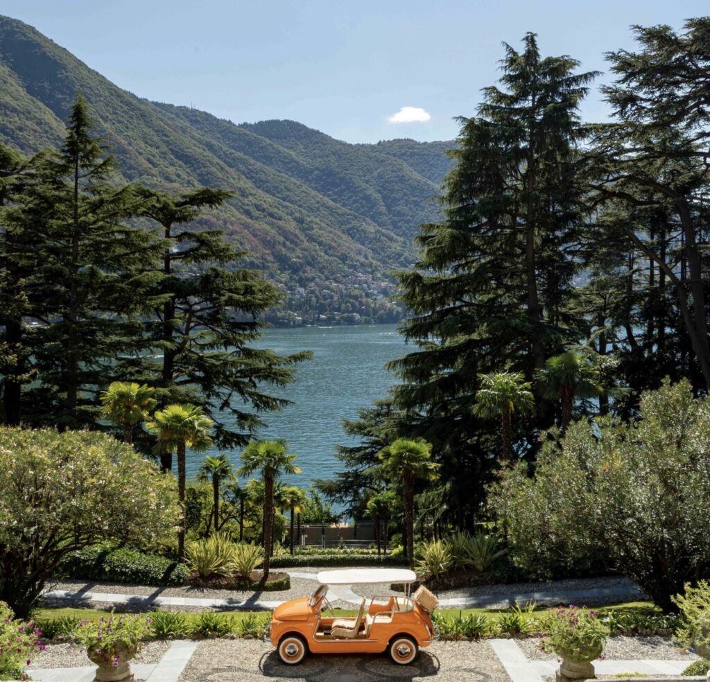 An orange golf cart parked on a garden path on Lake Como – perfect for a luxurious wedding under a bright blue sky.