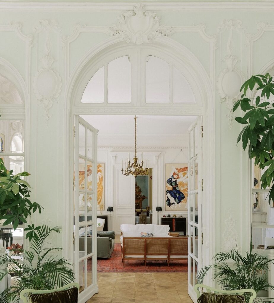 Ein elegantes Wohnzimmer mit großen Torbögen, Kronleuchtern, Zimmerpflanzen und farbenfrohen Kunstwerken an den Wänden – eine Atmosphäre, die an die Villa Rocabella erinnert und perfekt für alle ist, die davon träumen, im Stil der Côte d’Azur zu heiraten.