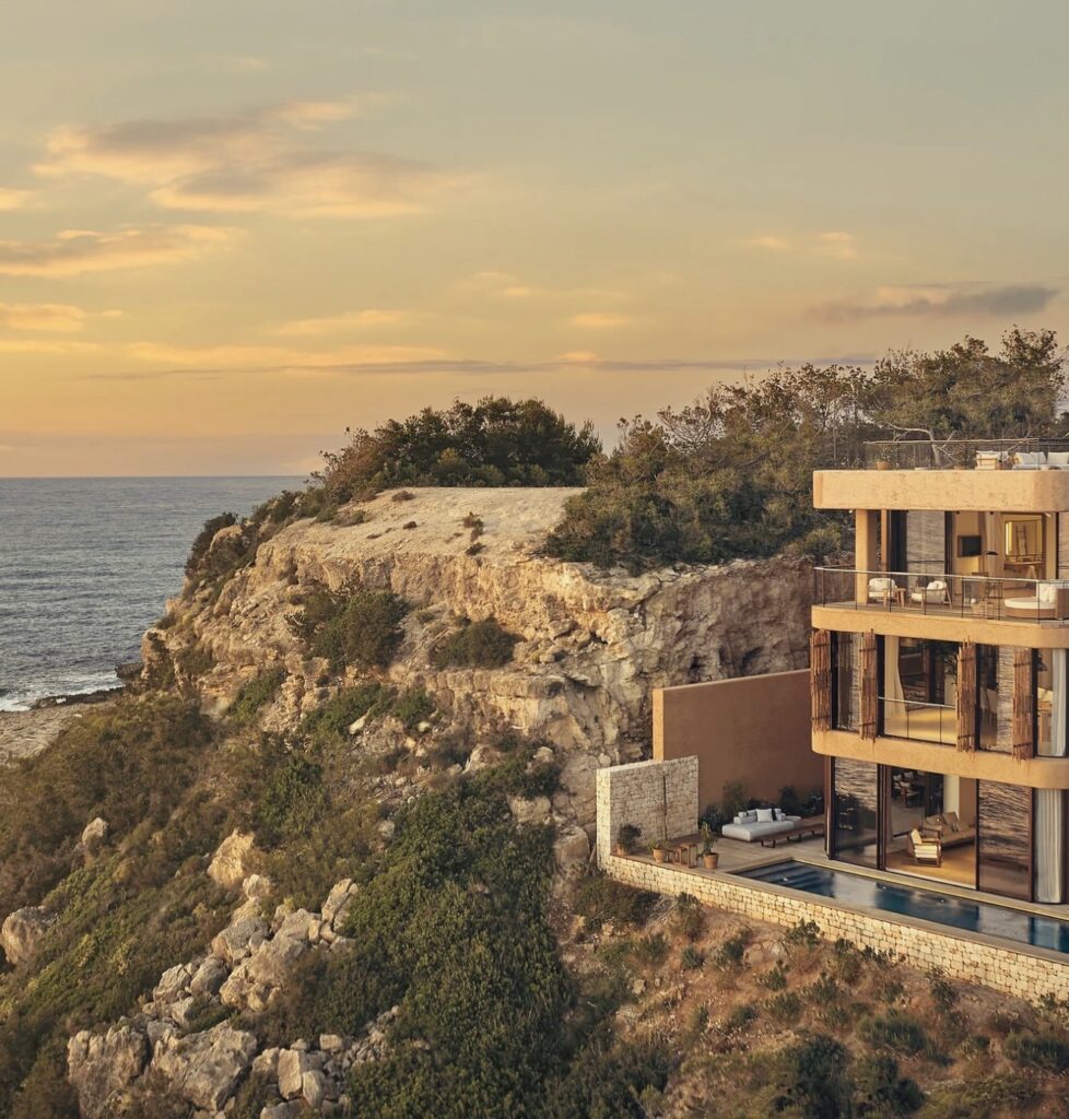 A multi-story villa with a swimming pool on a rocky cliff overlooking a luxurious wedding venue.