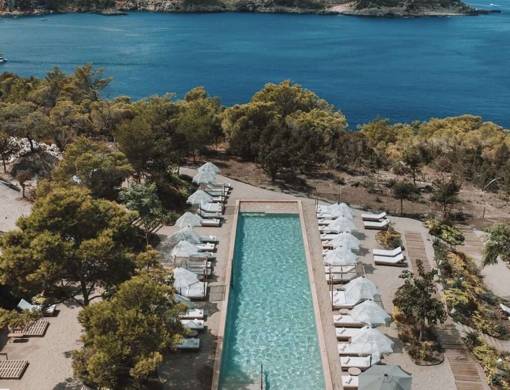 Rectangular pool with sun loungers and umbrellas overlooking a wedding venue on Ibiza.
