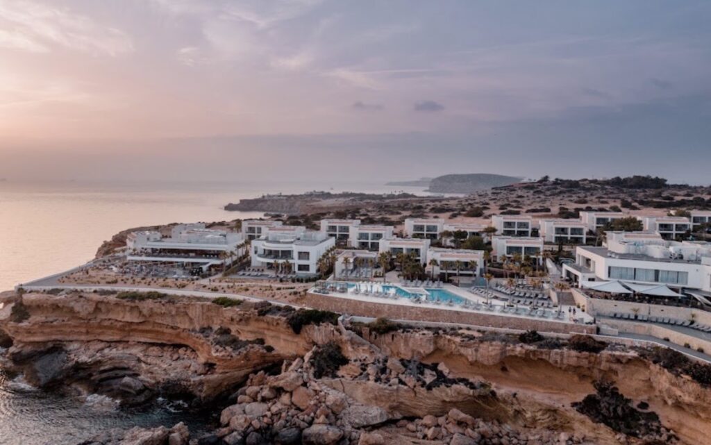 Aerial view of a luxurious wedding resort on a rocky cliff at sunset.