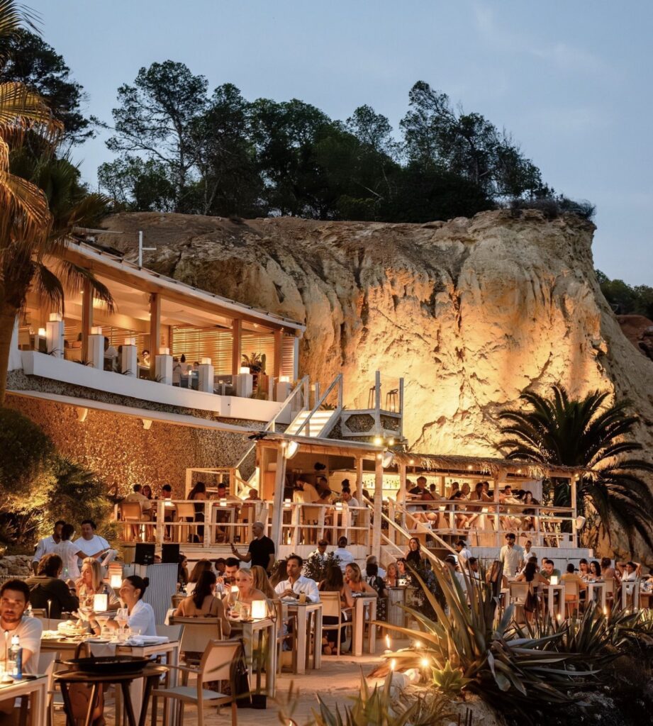 Guests enjoy a dinner during a luxurious wedding in a breathtaking setting on the terrace of a restaurant that is built into a cliff wall.