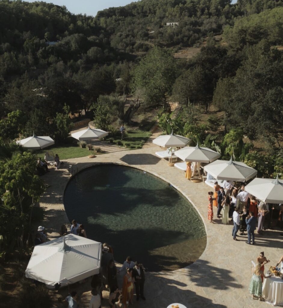 Guests at a luxurious outdoor wedding at the pool amidst a wooded environment.