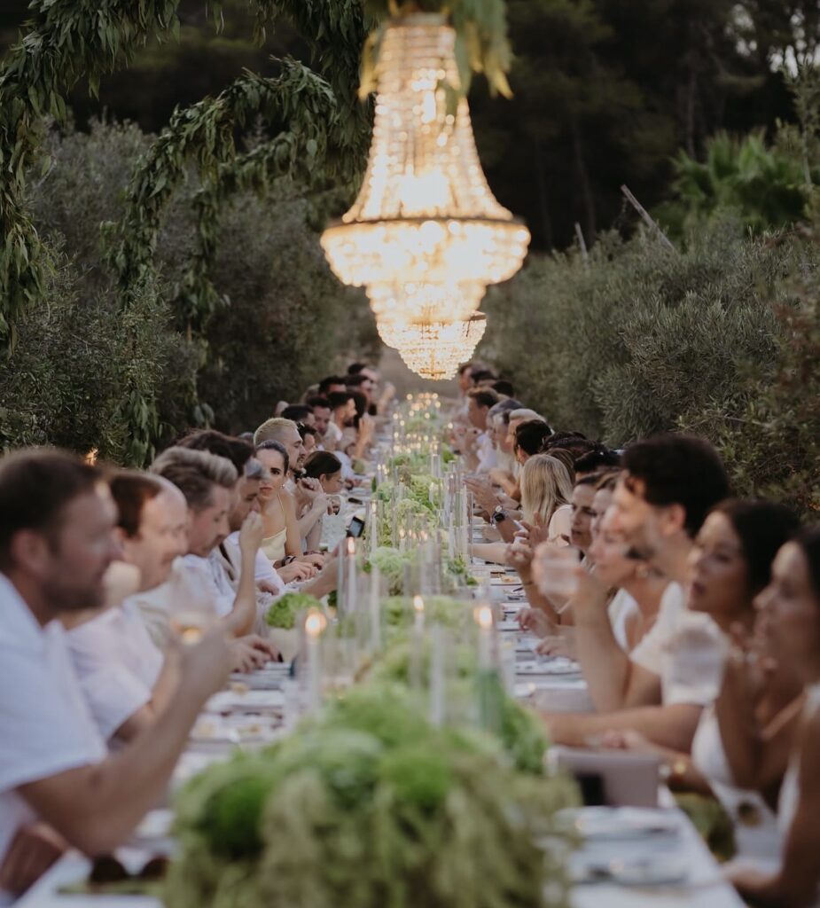 A long banquet table, set for a luxurious wedding feast in a special location under a crystal chandelier.